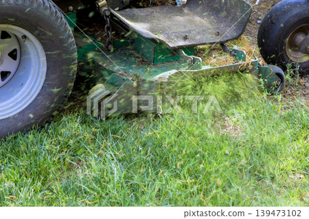 Lawnmower cuts grass in backyard while grass clippings scatter around Lawnmower cuts grass in backyard while grass clippings scatter around 139473102