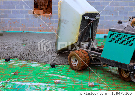Wheelbarrow bucket is pouring concrete on construction site workers prepare ground using tools Wheelbarrow bucket is pouring concrete on construction site workers prepare ground using tools 139473109