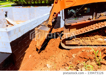 Excavator moves soil next to construction site where building foundation Excavator moves soil next to construction site where building foundation 139473126