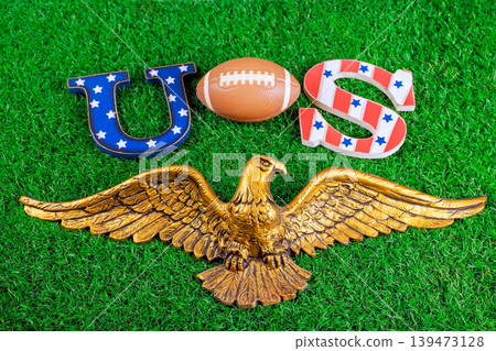 American football sits among US letters golden eagle on green grass, super bowl sports for an event. American football sits among US letters golden eagle on green grass, super bowl sports for an event. 139473128
