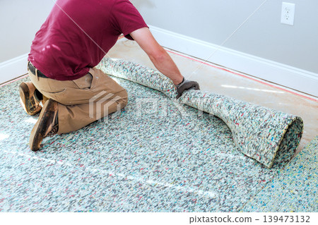 Contractor kneels on floor to roll up piece of carpet while renovating room in house. 139473132