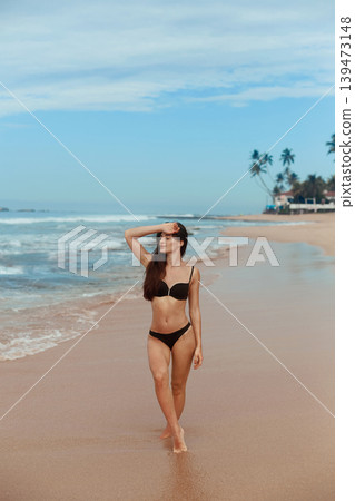 Beautiful woman in swimwear with copy space on the beach. Portrait of pretty girl with slim tanned sexy body in black bikini enjoying life. Summer lifestyle. Vacation Beautiful woman in swimwear with copy space on the beach. Portrait of pretty girl with slim tanned sexy body in black bikini enjoying life. Summer lifestyle. Vacation 139473148