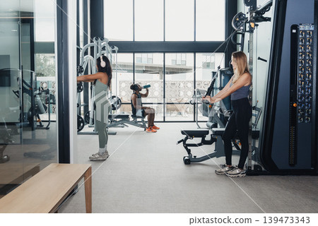 Ladies Converse While Working Out. Female Friends Gather And Talk During Fitness Session Breaks. Women Pause Their Workouts To Chat And Review Their Exercise Techniques Together Ladies Converse While Working Out. Female Friends Gather And Talk During Fitness Session Breaks. Women Pause Their Workouts To Chat And Review Their Exercise Techniques Together 139473343