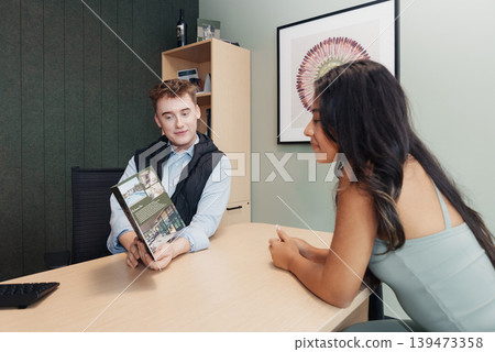 Agent Showing Brochure To Client, Office Consultation Focused On Property Listing Details, Agent Explaining Features With Gestures, Brochures And Laptop On Desk, Collaborative Agent Showing Brochure To Client, Office Consultation Focused On Property Listing Details, Agent Explaining Features With Gestures, Brochures And Laptop On Desk, Collaborative 139473358
