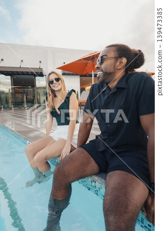 Man And Woman Bonding Casually Near Swimming Pool With Sunglasses. Two Individuals Exchanging Relaxed Conversations Beside Pool With Casual Attire And Modern City Backdrop Man And Woman Bonding Casually Near Swimming Pool With Sunglasses. Two Individuals Exchanging Relaxed Conversations Beside Pool With Casual Attire And Modern City Backdrop 139473385