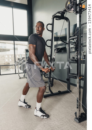 Black Man Athlete Performing Cable Rotation. Corefocused Exercise With Cable Pulley, Controlled Twist, Resistance Tension, Defined Obliques, Modern Gym Backdrop, Concentrated Expression, Black Man Athlete Performing Cable Rotation. Corefocused Exercise With Cable Pulley, Controlled Twist, Resistance Tension, Defined Obliques, Modern Gym Backdrop, Concentrated Expression, 139473414