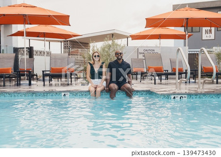 Two Friends Sitting Pool Edge Together, Bright Umbrellas And Resort Chairs Framing Clear Water Reflection, Urban Apartment Backdrop, Weekend Leisure And Smiling Candid Portrait, Modern Two Friends Sitting Pool Edge Together, Bright Umbrellas And Resort Chairs Framing Clear Water Reflection, Urban Apartment Backdrop, Weekend Leisure And Smiling Candid Portrait, Modern 139473430