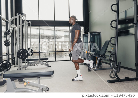 Black Man Influencer Pausing Between Sets. Casual Pose Near Cable Machine, Reflective Gaze, Headphones Around Neck, Athletic Shorts, Gym Skyline View Through Windows, Relaxed Confidence, Black Man Influencer Pausing Between Sets. Casual Pose Near Cable Machine, Reflective Gaze, Headphones Around Neck, Athletic Shorts, Gym Skyline View Through Windows, Relaxed Confidence, 139473450