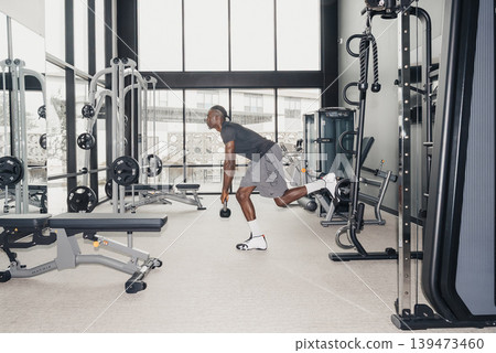 Black Man Athlete Executing Singleleg Deadlift. Controlled Movement With Dumbbell, Hamstring Engagement, Hip Hinge Mechanics, Core Stabilization, Quiet Gym Environment, Large Windows, 139473460
