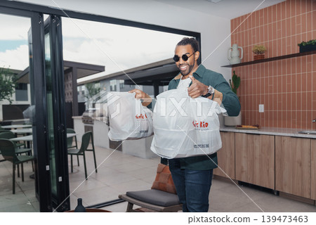 Delivery With Style. Courier Displaying Custom Bags Confidently In Kitchen Setting. Delivery Person Showcasing Branded Packaging With Vibrant Energy In Contemporary Kitchen Delivery With Style. Courier Displaying Custom Bags Confidently In Kitchen Setting. Delivery Person Showcasing Branded Packaging With Vibrant Energy In Contemporary Kitchen 139473463