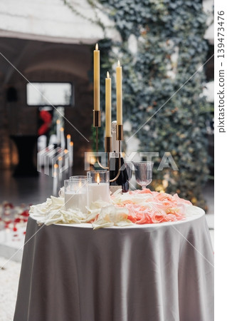 Elegant Candlelit Wedding Table Set With Gold Candelabra, Glassware, Blush Rose Petals Scattered Over Grey Linen, Ivycovered Wall Backdrop, Soft Natural Light Creating Warm Glow, Intimate Elegant Candlelit Wedding Table Set With Gold Candelabra, Glassware, Blush Rose Petals Scattered Over Grey Linen, Ivycovered Wall Backdrop, Soft Natural Light Creating Warm Glow, Intimate 139473476