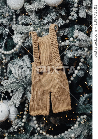 Knitted Baby Romper Hanging On Tree, Flocked Branches And Pearl Garland, Warm Fairy Lights And Soft Bokeh, Handcrafted Neutral Ornament Evokes Cozy Holiday Reveal And Gift Inspiration Knitted Baby Romper Hanging On Tree, Flocked Branches And Pearl Garland, Warm Fairy Lights And Soft Bokeh, Handcrafted Neutral Ornament Evokes Cozy Holiday Reveal And Gift Inspiration 139473503