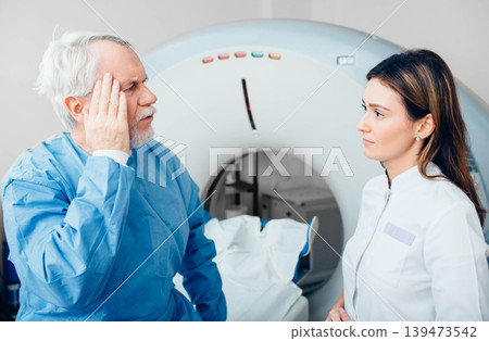 Senior patient complaint of head pain to his doctor while sitting on scanner table. 139473542