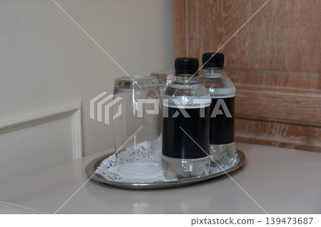Two bottled waters, glass on tray in hotel room interior with clean minimalist arrangement on table. Hospitality service, travel accommodation, hotel amenities, guest comfort, lifestyle Two bottled waters, glass on tray in hotel room interior with clean minimalist arrangement on table. Hospitality service, travel accommodation, hotel amenities, guest comfort, lifestyle 139473687