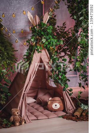 Cozy children's teepee tent in a fairytale forest interior with toys and fairy lights 139473892