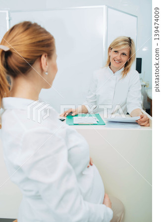 Smiling obstetrician talking with pregnant woman in clinic examination room Smiling obstetrician talking with pregnant woman in clinic examination room 139474009