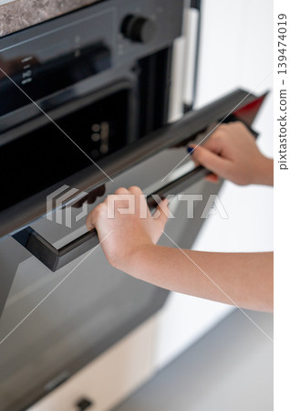 A hands open the door of a modern built-in oven. Concept of home cooking and appliance use. 139474019