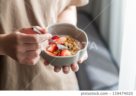 Close-up of a person holding a ceramic bowl with yogurt, fresh strawberries, and granola. 139474020