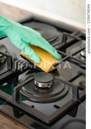 Cleaning a gas hob with a sponge and glove, removing grease in a modern kitchen. 139474044