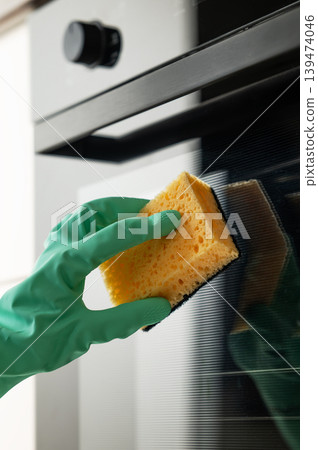 Cleaning the oven door with a sponge and a rubber glove, removing grease in a modern kitchen. 139474046