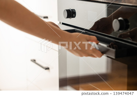 A hand open the door of a modern built-in oven. Concept of home cooking and appliance use. 139474047