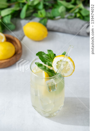 A summer drink with lemon, mint, and ice in a glass on a light background. A summer drink with lemon, mint, and ice in a glass on a light background. 139474052