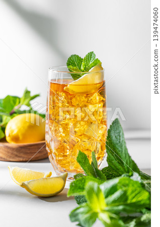 Iced tea with lemon and mint in a glass on a light background with shadows Iced tea with lemon and mint in a glass on a light background with shadows 139474060