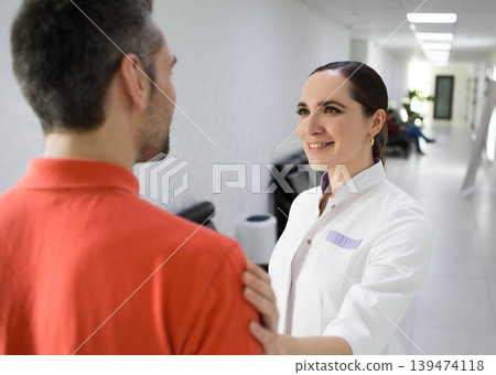 A healthcare provider engages in a friendly conversation with a patient in a well-lit clinic corridor, emphasizing personalized care A healthcare provider engages in a friendly conversation with a patient in a well-lit clinic corridor, emphasizing personalized care 139474118