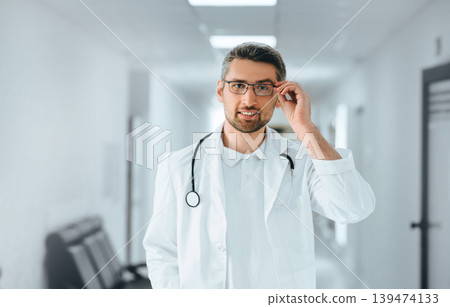 portrait of a clinical doctor adjusting his glasses at clinic corridor. portrait of a clinical doctor adjusting his glasses at clinic corridor. 139474133