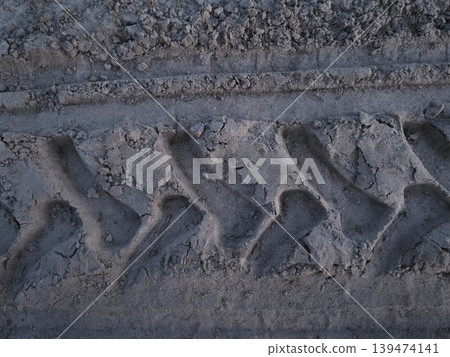 Close-up of deep tire tread mark on dry sandy ground with rough texture under natural light. Concept of off-road transportation and heavy machinery impact Close-up of deep tire tread mark on dry sandy ground with rough texture under natural light. Concept of off-road transportation and heavy machinery impact 139474141