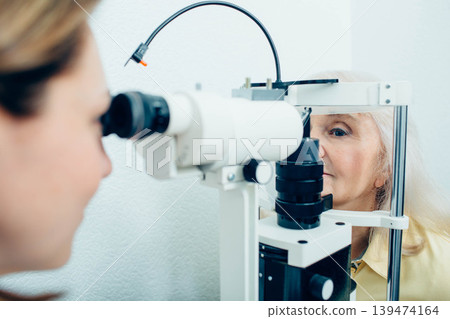 Senior woman doing eye test with eye equipment Senior woman doing eye test with eye equipment 139474164