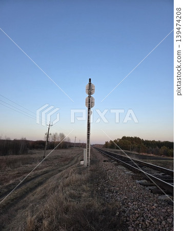 Railway tracks stretching into the distance with a tall signal pole against a clear evening sky and forest. Concept of industrial transportation and travel Railway tracks stretching into the distance with a tall signal pole against a clear evening sky and forest. Concept of industrial transportation and travel 139474208