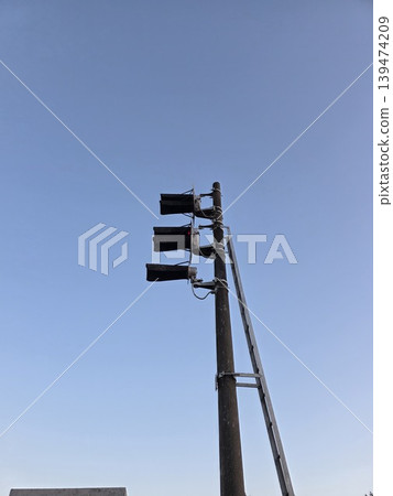 Close-up of a black railway signal with three lamps on a metal pole against a clear blue sky. Concept of safety and traffic control on the railway Close-up of a black railway signal with three lamps on a metal pole against a clear blue sky. Concept of safety and traffic control on the railway 139474209