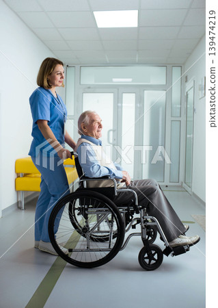 friendly nurse pushing senior patient in wheelchair at hospital corridor friendly nurse pushing senior patient in wheelchair at hospital corridor 139474219