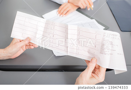 Senior patient looking at the results of a cardiogram of heart in a cardiologist's office. Diagnostics and treatment of arrhythmias, coronary heart disease, and heart failure Senior patient looking at the results of a cardiogram of heart in a cardiologist's office. Diagnostics and treatment of arrhythmias, coronary heart disease, and heart failure 139474333