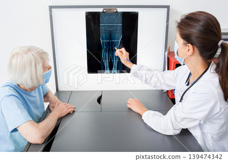 Rheumatologist consulting an elderly patient by pointing to X-ray of knee joint. Arthritis and disease of the joints of the legs Rheumatologist consulting an elderly patient by pointing to X-ray of knee joint. Arthritis and disease of the joints of the legs 139474342