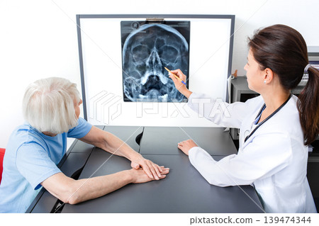 Doctor consider and discuss with senior patient X-ray of her head and maxillary sinuses. Diagnostics and treatment of sinusitis and frontal sinusitis 139474344