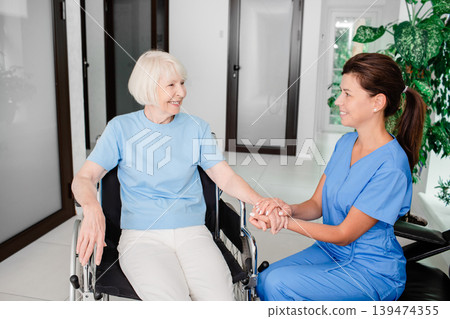 Smiling nurse and elderly woman patient in a wheelchair. Medical care for people with disabilities Smiling nurse and elderly woman patient in a wheelchair. Medical care for people with disabilities 139474355