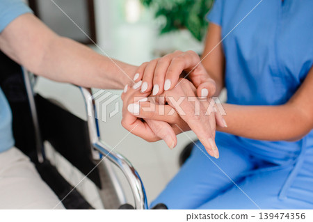 Medical support patient in a wheelchair. Close-up of hands of a healthcare worker and an elderly person with a disability taking care of a patient Medical support patient in a wheelchair. Close-up of hands of a healthcare worker and an elderly person with a disability taking care of a patient 139474356
