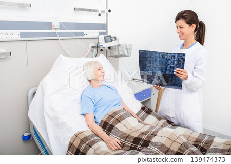 Experienced doctor holding X-ray of spine of an elderly woman. Patient and the doctor are smiling because the woman's spine health is fine. Treatment of spine disease, osteochondrosis 139474373