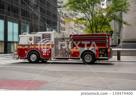 New york, usa august 17,2024. Fdny red and white fire truck parked curbside in manhattan with american flag reflected in a nearby building window, daytime New york, usa august 17,2024. Fdny red and white fire truck parked curbside in manhattan with american flag reflected in a nearby building window, daytime 139474400