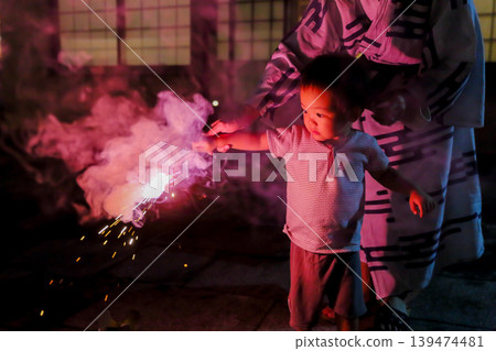 一個孩子表情嚴肅地欣賞著他人生中的第一支手持煙火。 一個孩子表情嚴肅地欣賞著他人生中的第一支手持煙火。 139474481