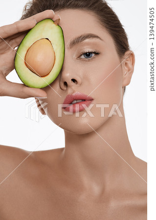 Moisturizing and care for skin using cosmetics with avocado. Woman holds avocado near her fresh glowing hydrated skin face 139474505