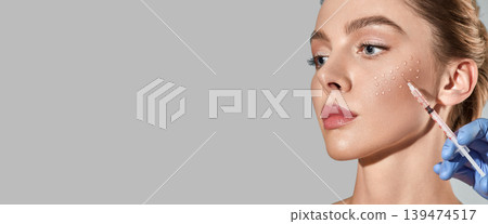Biorevitalization procedure. Pretty woman while beauty injections with hyaluronic acid for smoothing of mimic wrinkles around eyes, over grey background with space for text 139474517