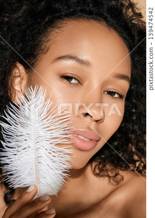Facial skin care. African American woman showing smooth and soft her skin is by touching her face with white feather Facial skin care. African American woman showing smooth and soft her skin is by touching her face with white feather 139474542