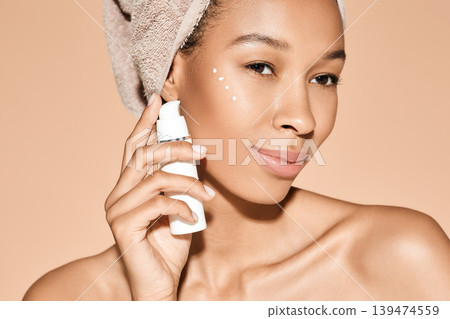 Positive curly woman applies moisturizing cream on her face, on beige background. Face cream moisturizing skin, skincare Positive curly woman applies moisturizing cream on her face, on beige background. Face cream moisturizing skin, skincare 139474559
