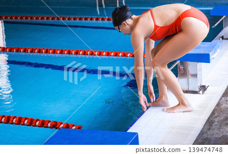 Female professional swimmer getting ready to jump in swimming pool of starting position. Jumping in a swimming pool, training Female professional swimmer getting ready to jump in swimming pool of starting position. Jumping in a swimming pool, training 139474748