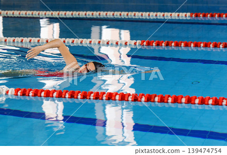 Young woman swimmer is swimming in the pool. Freestyle stroke, front crawl stroke. Swimming in blue pool, side view Young woman swimmer is swimming in the pool. Freestyle stroke, front crawl stroke. Swimming in blue pool, side view 139474754