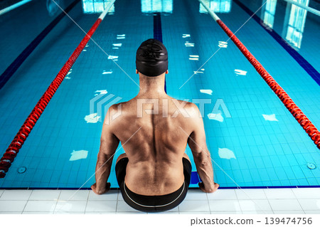 Swimmer sitting at the poolside, back view. Professional swimmer near the swimming pool, hard contrast Swimmer sitting at the poolside, back view. Professional swimmer near the swimming pool, hard contrast 139474756