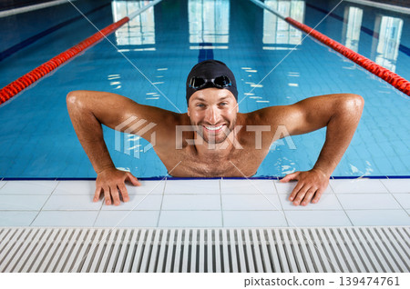 A professional swimmer man emerges from the swimming pool and looking at camera. Portrait of a swimmer at pool side A professional swimmer man emerges from the swimming pool and looking at camera. Portrait of a swimmer at pool side 139474761
